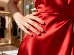 Dłoń z letnim manicure w odcieniach koralu, turkusu i żółci na tle piaszczystej plaży oraz morskich fal.